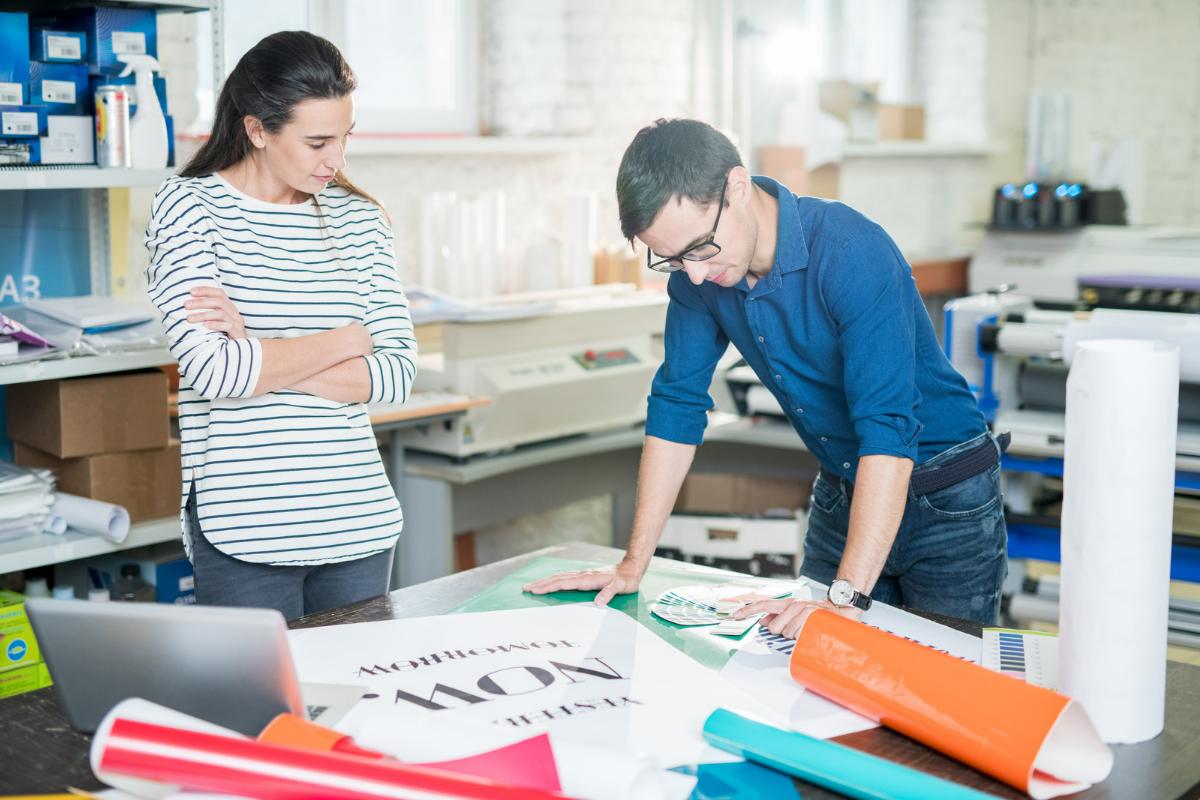 two people in printing company looking at large poster on table